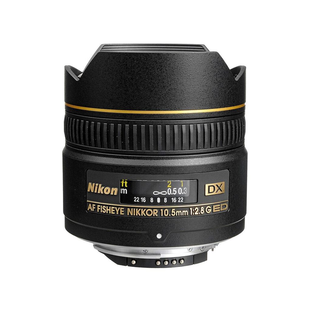 af-s_dx_nikkor_10_5_f2_8_if-ed_0001 Nikon AF-S DX Nikkor Fisheye 10.5mm f/2.8G IF-ED -objektiivi seisoo pystyasennossa valkoisella taustalla, ja sen kultainen merkintä, tarkennusrengas ja etäisyysasteikko korostuvat.