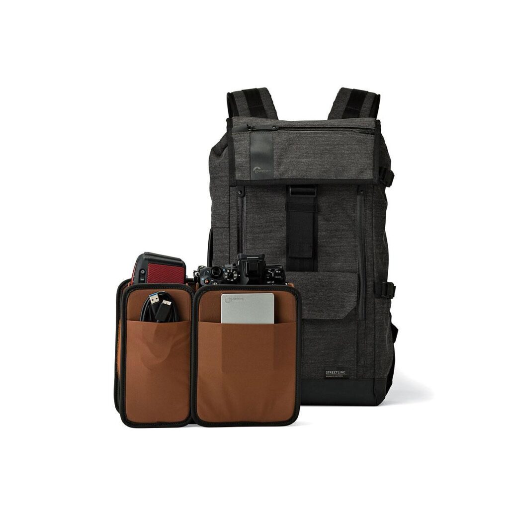 Lowepro_Streetline_BP_250_001 Mustan ja harmaan värinen Lowepro Streetline PB 250 - Limited Edition -laukku seisoo pystyssä valkoisella pohjalla, ja sen etutasku on avattu, jolloin esiin paljastuu ruskeat irrotettavat insertit, joihin mahtuu kamera, kuulokkeet, pieni tabletti ja elektroniset tarvikkeet.