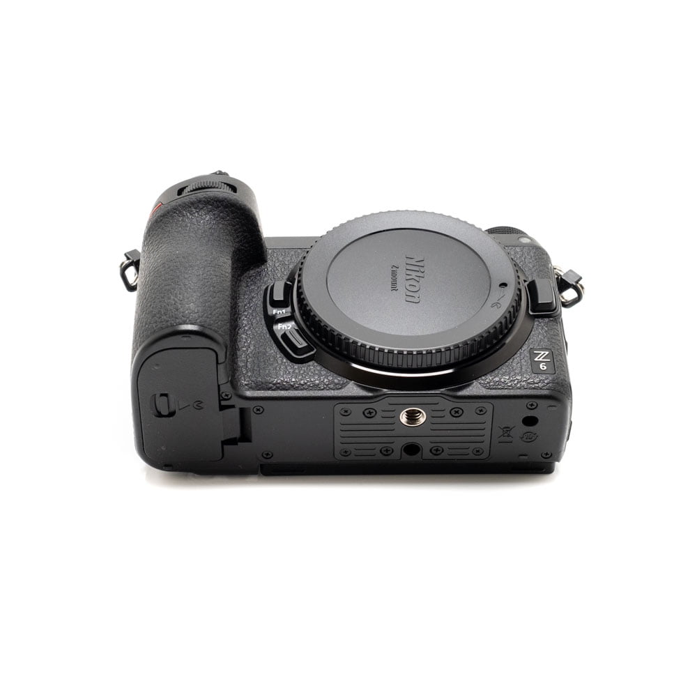 Käytetty musta Nikon Z6 II (Kunto K5, Takuuta 22kk, Shuttercount 1100) -kamerarunko on kuvattu selällään makaavana, jolloin objektiivin kiinnityssuoja, kuvioitu kahva sekä eri portit ja pohjan ruuvikiinnikkeet tulevat esiin.