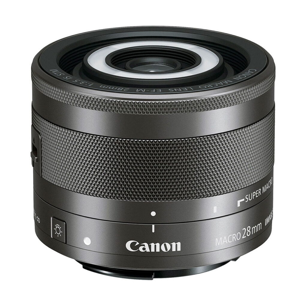 Canon_EF-M_28mm_f_3_5_Macro_IS_STM_001 Canon EF-M 28mm f/3.5 Macro IS STM -objektiivi, jossa on kuvioitu tarkennusrengas ja jossa on merkinnät "Canon MACRO 28mm" ja "SUPER MACRO", näkyy valkoista taustaa vasten.