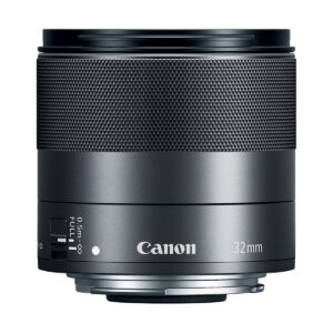 Canon_EF-M_32mm_f_1_4_STM_002 Lähikuva Canon EF-M 32mm f/1.4 STM -objektiivista, jossa korostuvat tarkennusrengas, säätökytkin ja Canon-brändi valkoisella taustalla.