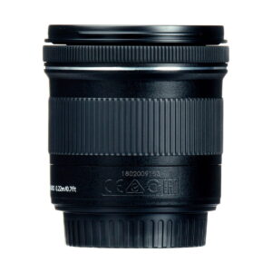 Canon_EF-S_10-18mm_f_4-5_6_IS_STM_003 Lähikuva Canon EF-S 10-18mm f/4.5-5.6 IS STM -objektiivista näyttää sen mustat, kuvioidut tarkennusrenkaat ja zoomausrenkaat, joissa on valkoisia merkintöjä ja symboleja lähellä pohjaa, kaikki valkoista taustaa vasten.