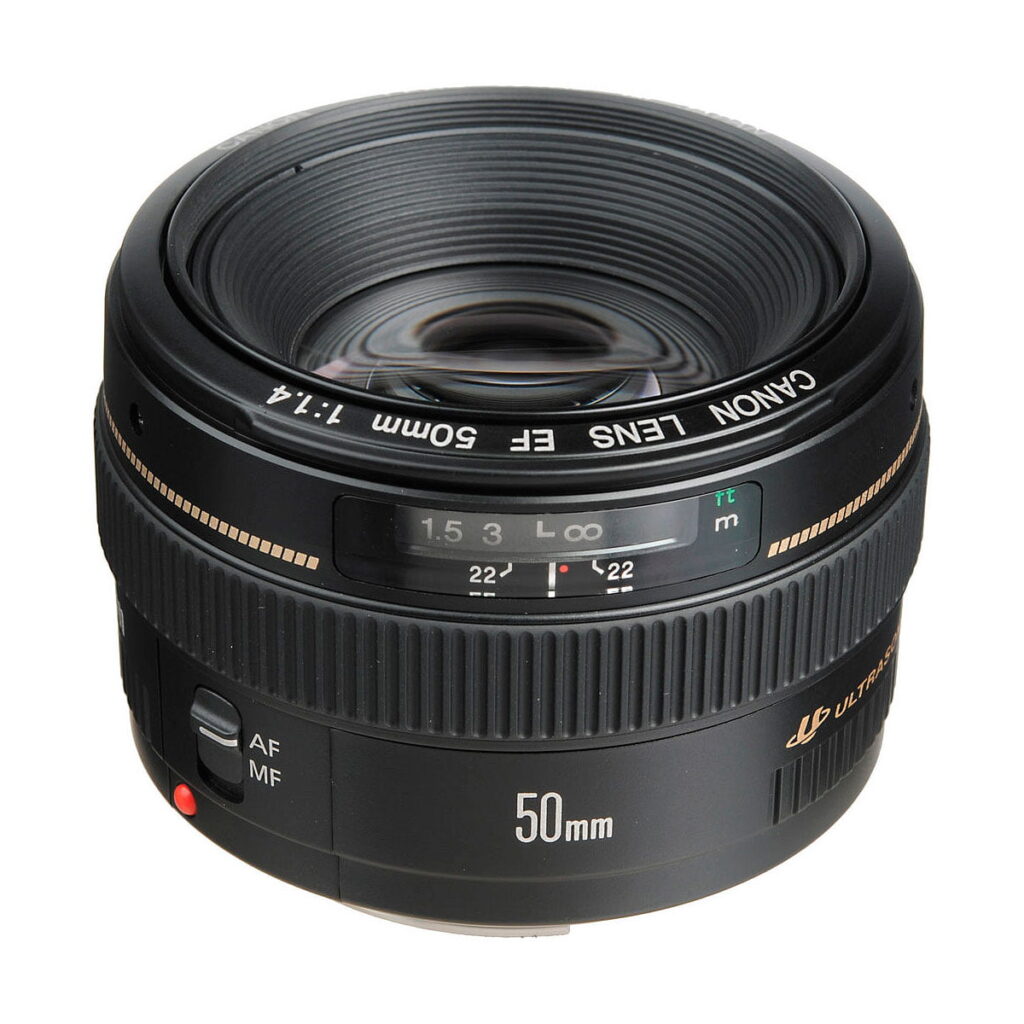 Canon_EF_50mm_f_1_4_USM_002 A Canon EF 50mm f/1.4 USM lens, with black body and distance scale window, is visible from an angle to highlight the glass and markings. The lens has automatic and manual focus switches.
