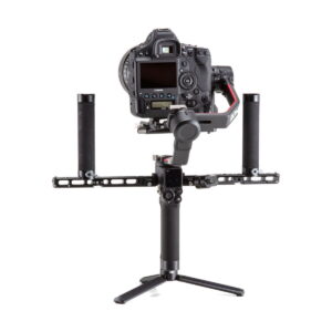 DJI-R-Twist-Grip-Dual-Handle-for-RS-2-RSC-04 The professional DSLR camera is attached to the DJI R Twist Grip Dual Handle for RS 2 & RSC 2, which is attached to a handheld gimbal and rests on a small stand against a white background.