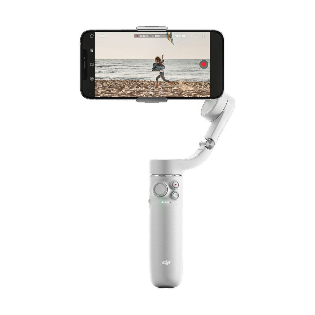 DJi_OM_5_Sunset_Grey_002 A DJI OM 5 vakaaja älypuhelimille - Harmaa pitää puhelinta, jossa näkyy video rannalla juoksevasta henkilöstä. Vakaajassa on ohjauspaneeli painikkeilla ja joystickilla.