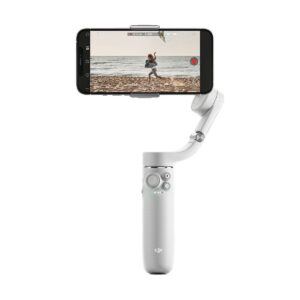 DJi_OM_5_Sunset_Grey_002 A DJI OM 5 vakaaja älypuhelimille - Harmaa pitää puhelinta, jossa näkyy video rannalla juoksevasta henkilöstä. Vakaajassa on ohjauspaneeli painikkeilla ja joystickilla.