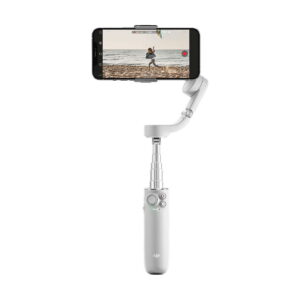 DJi_OM_5_Sunset_Grey_003 Älypuhelin on kiinnitetty DJI OM 5 vakaaja älypuhelimille - Harmaa, kuvassa laajennettu ja tallentava video henkilöstä, joka juoksee rannalla.