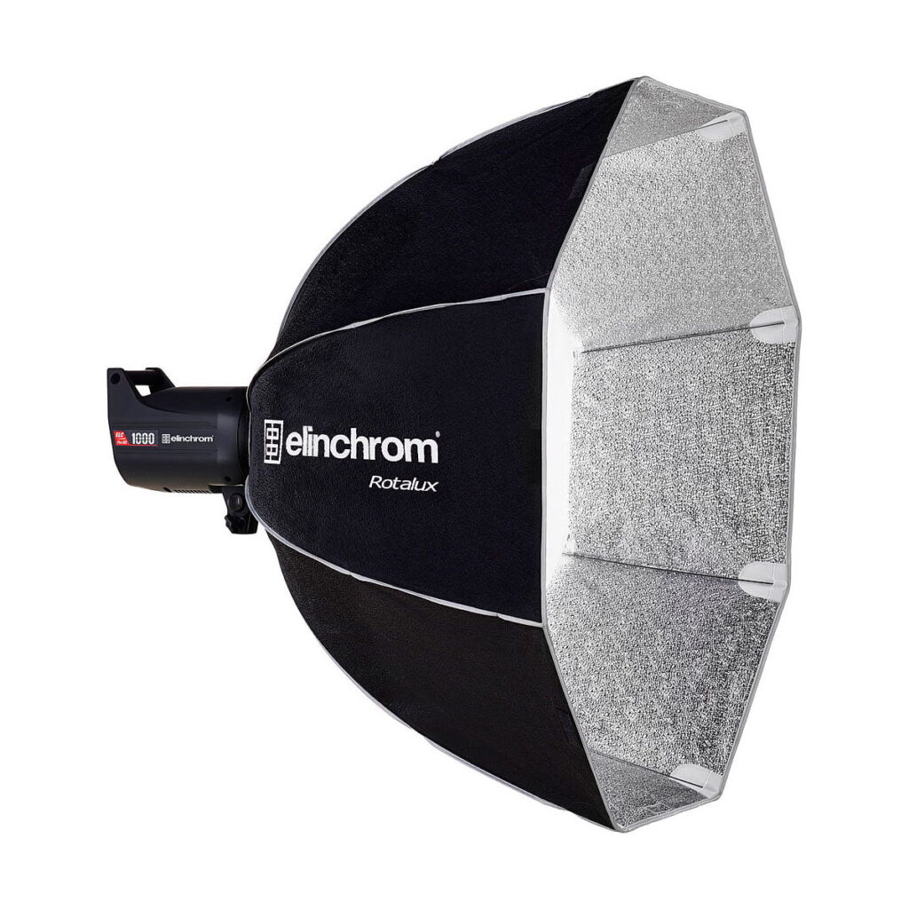 Elinchrom_Rotalux_Deep_Octabox_100cm_003 Elinchrom Rotalux Deep Octabox 100cm, musta softbox-valomodifiointilaite, jossa on hopeinen sisäpuoli, näkyy asennettuna studiostroboskooppivalaisimeen valkoista taustaa vasten.