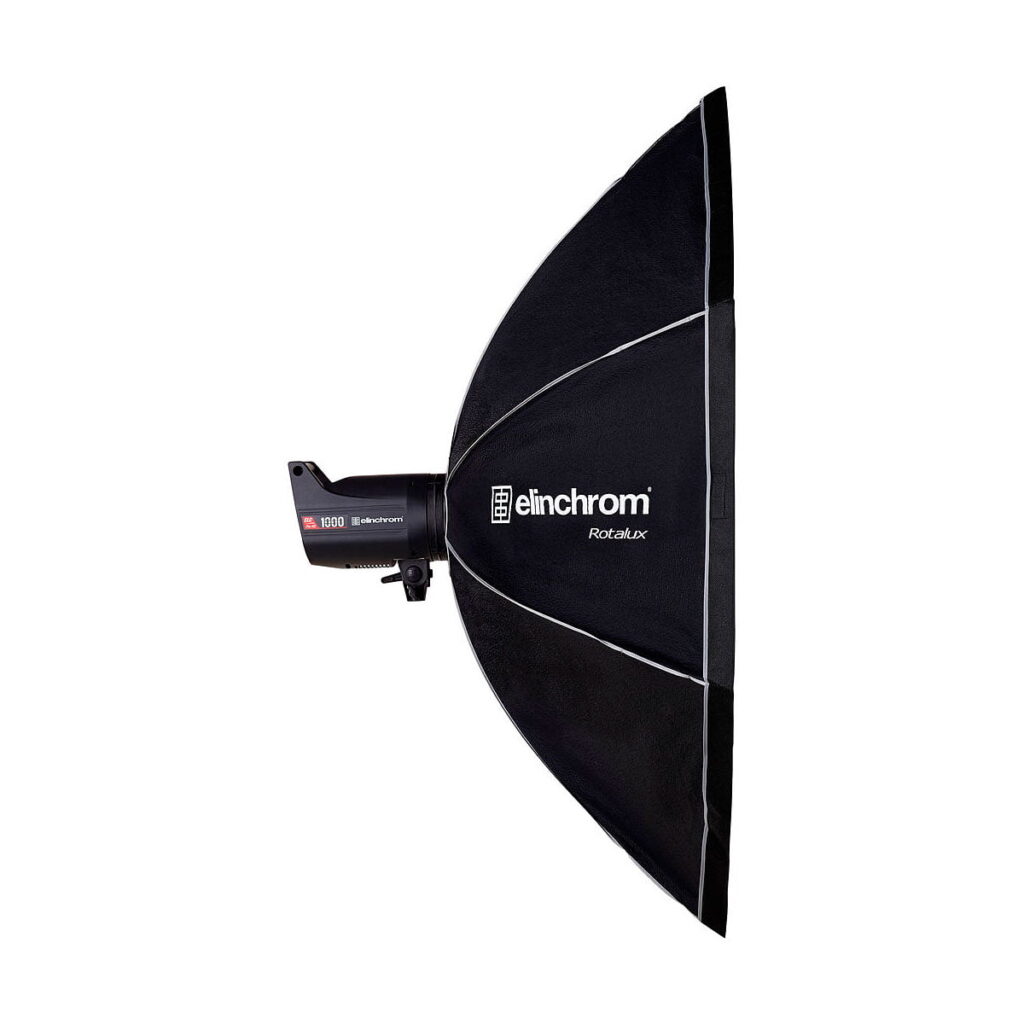Elinchrom_Rotalux_Octabox_135cm_002 Studiostroboskooppivalaisin, johon on kiinnitetty suuri musta Elinchrom Rotalux Octabox 135cm softbox, kuvattuna sivulta valkoista taustaa vasten.