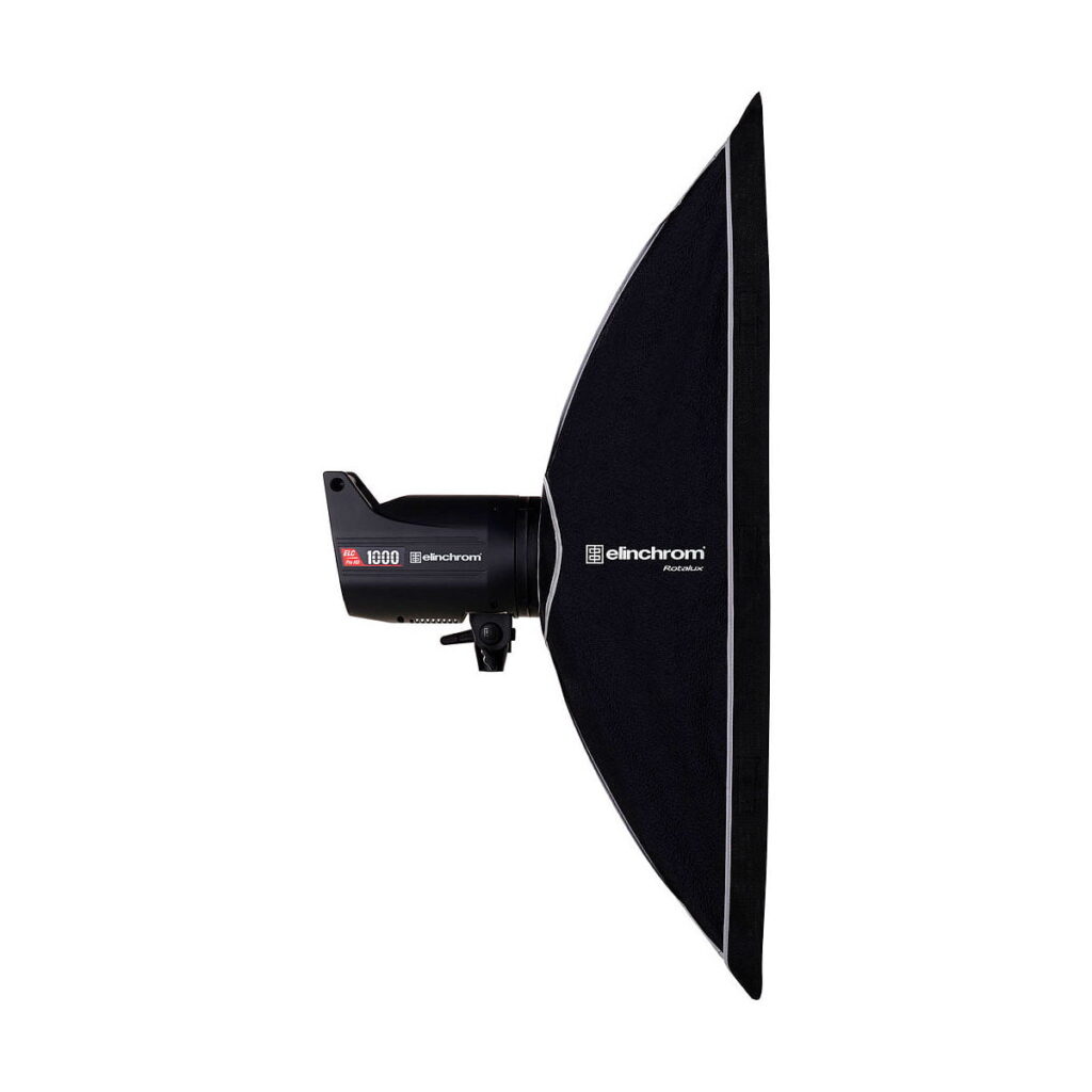 Elinchrom_Rotalux_Stripbox_35x90cm_002 Mustaa Elinchrom Rotalux Stripbox 35x100cm -studiostroboskooppivalaisinta näytetään sivulta, kun siihen on kiinnitetty suorakulmainen softbox valkoista taustaa vasten.