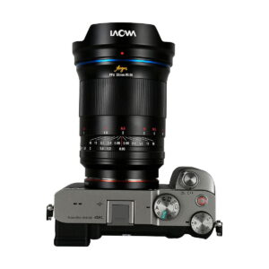 Laowa_Argus_35mm_f_0_95_FF-Sony-E_007 Ylhäältä katsottuna hopeinen digitaalikamera, jossa on säätöpyörät, painikkeet ja kuvioitu oikea kahva, johon on kiinnitetty suuri Laowa Argus 35mm f/0.95 FF - Sony-E -objektiivi.