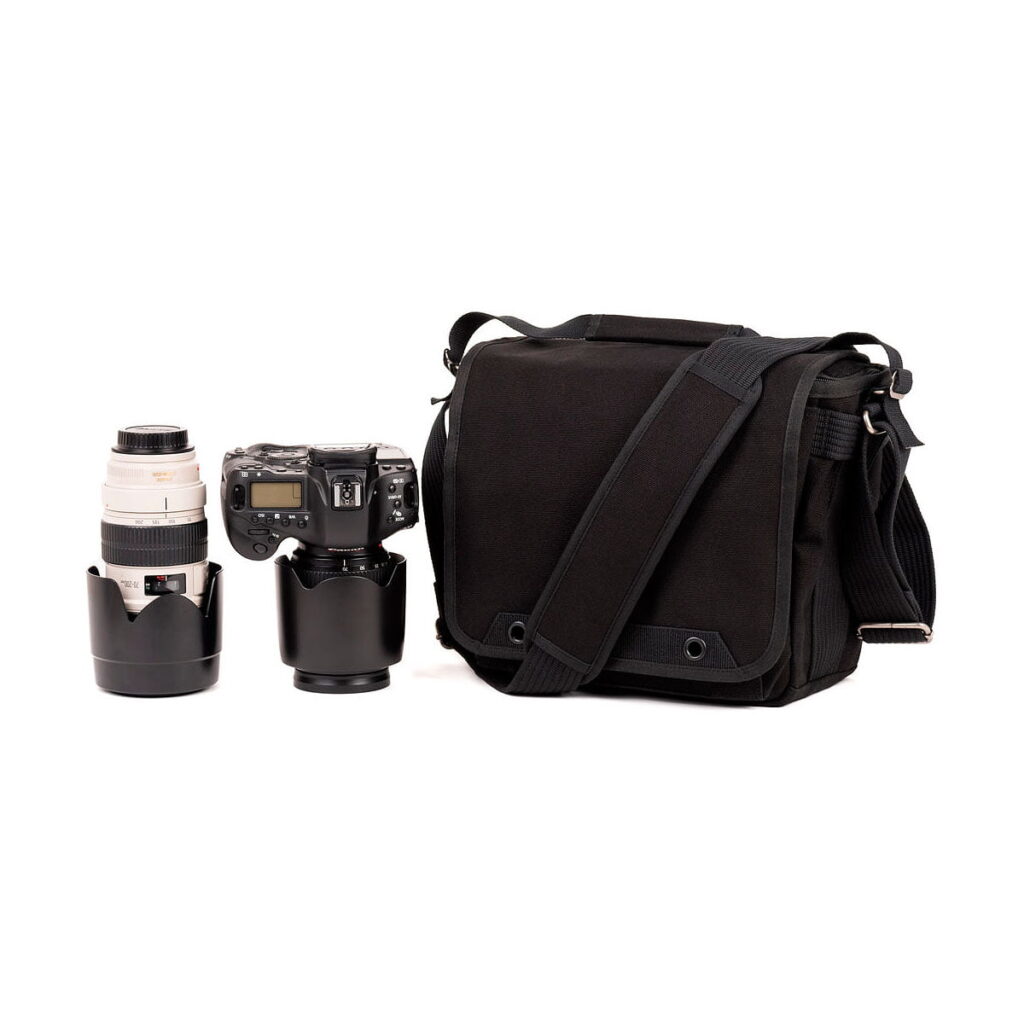 Think_Tank_Retrospective_10_V2_0-Musta_003 A Think Tank Retrospective 10 V2.0 - A black camera bag stands next to a digital camera with a lens attached and a separate telephoto lens, all upright against a white background.