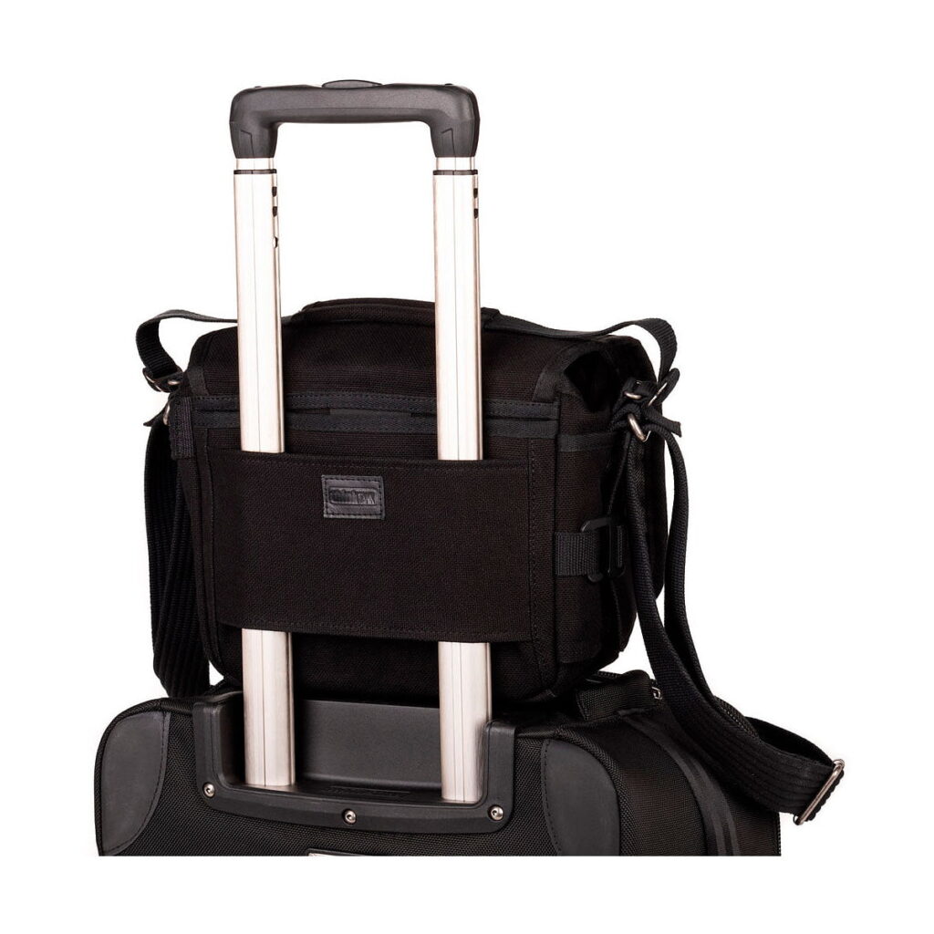 Think_Tank_Retrospective_5_V2_0-Musta_005 Think Tank Retrospective 5 V2.0 - Black, a compact black bag with a shoulder strap is securely attached to the extended handle of a larger roller bag against a white background.