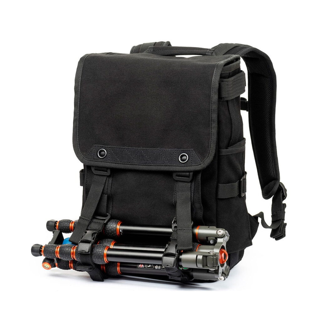 Think_Tank_Retrospective_Backpack_15-Black_007 Think Tank Retrospective Backpack 15, black with padded shoulder straps and front flap, has a tripod attached to the front with two adjustable buckle straps. The background is white.