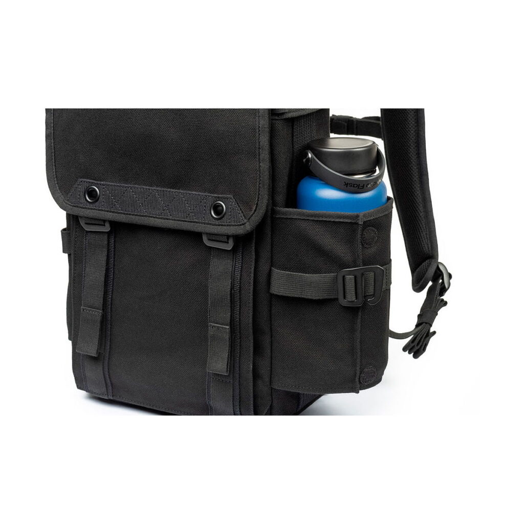 Think_Tank_Retrospective_Backpack_15-Black_009 Close-up Think Tank Retrospective Backpack 15, black, with blue water bottle in side pocket held by adjustable strap. The black backpack has buttoned flaps and durable fabric.