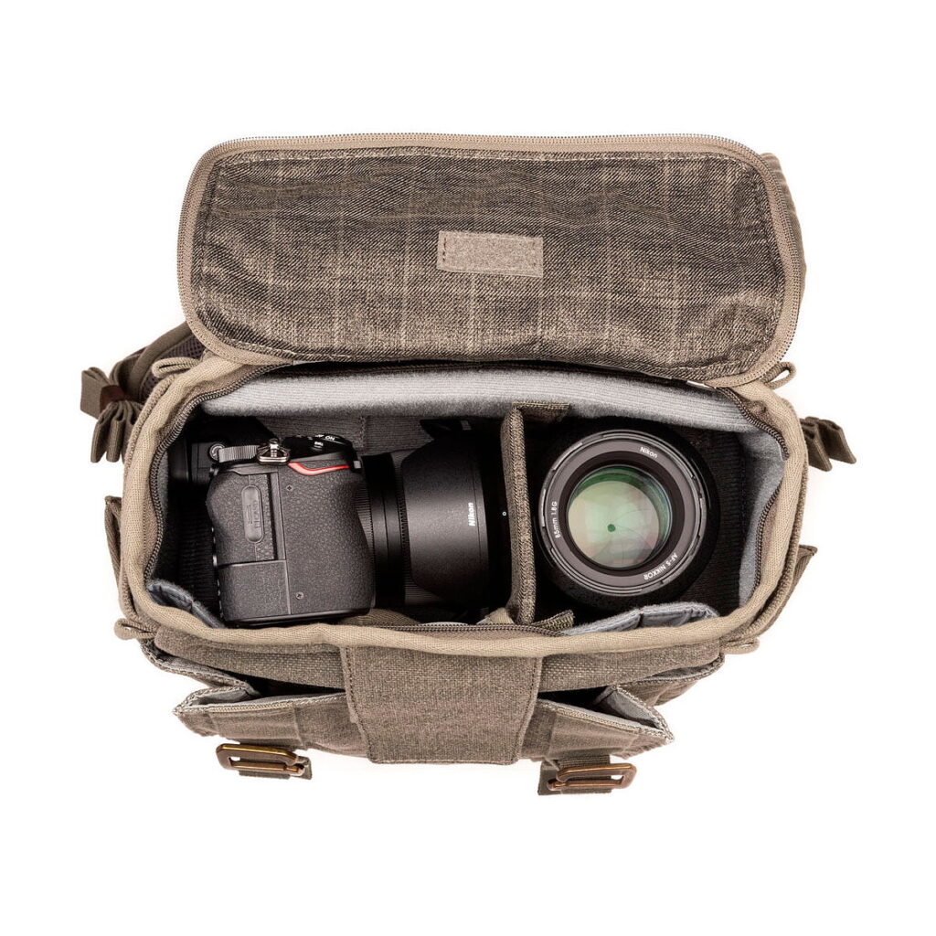 Ylhäältä katsottuna Think Tank Retrospective Backpack 15 -kamerareppu, pinestone, avattuna niin, että pehmustetut lokerot, joihin mahtuu vasemmalla DSLR-kameran runko ja objektiivi ja oikealla suuri kameran objektiivi.