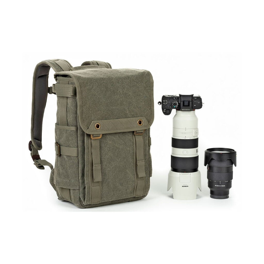 Think Tank Retrospective Backpack 15 -kamerareppu, pinestone, näkyy ammattilaiskameran vieressä, jossa on teleobjektiivi ja ylimääräinen objektiivi, kaikki valkoista taustaa vasten.