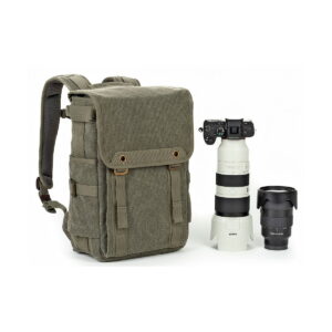 Think Tank Retrospective Backpack 15 -kamerareppu, pinestone, näkyy ammattilaiskameran vieressä, jossa on teleobjektiivi ja ylimääräinen objektiivi, kaikki valkoista taustaa vasten.