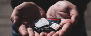 Henkilö pitää kädessään useita erikokoisia ja -merkkisiä SD- ja microSD-kortteja, ja yksi kirkas muovikotelo on näkyvissä korttien joukossa.
