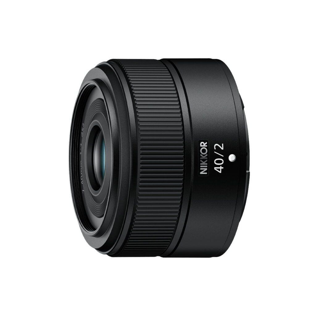 nikon_nikkor_z_40mm_f2_01 Nikon Nikkor Z 40mm f/2 -objektiivi näkyy mustana valkoista taustaa vasten, hieman vasemmalle suunnattuna. Objektiivissa on kuvioidut renkaat tarkkaa tarkennusta ja ohjausta varten.