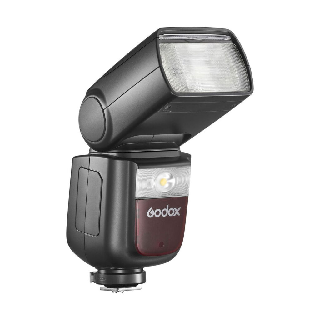 Godox-Ving-V860-III-TTL---Nikon-5 Musta Godox Ving V860 III TTL-salama Nikon-kameroille, jossa on suorakulmainen, ylöspäin taivutettu pää, läpikuultava kansi, ohjauspainikkeet ja jalkajalka, kuvassa valkoista taustaa vasten.