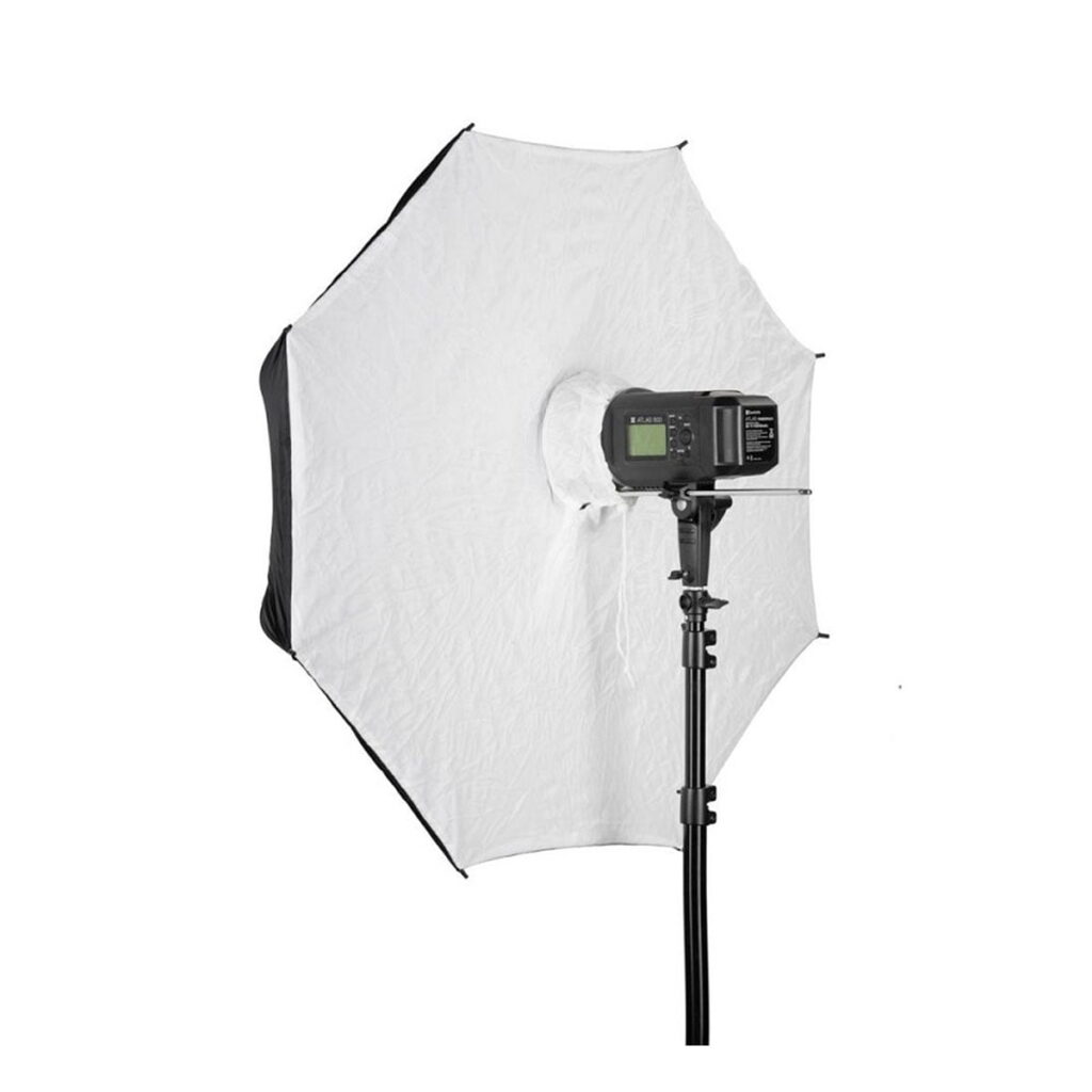 Quadralite_101_White_Umbrella_Softbox_004 Quadralite Umbrella Softbox 110cm, jossa on jalustalle asennettu digitaalinen salama, näkyy takaa valkoista taustaa vasten.