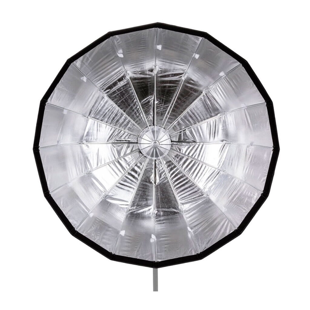 Quadralite Flex 105cm Foldable Beauty-Dish on suuri, pyöreä, hopeanvärinen heijastava sateenvarjo, jossa on segmentoitu metallinen sisus ja musta ulkoreuna, joka on suunniteltu valokuvaukseen.