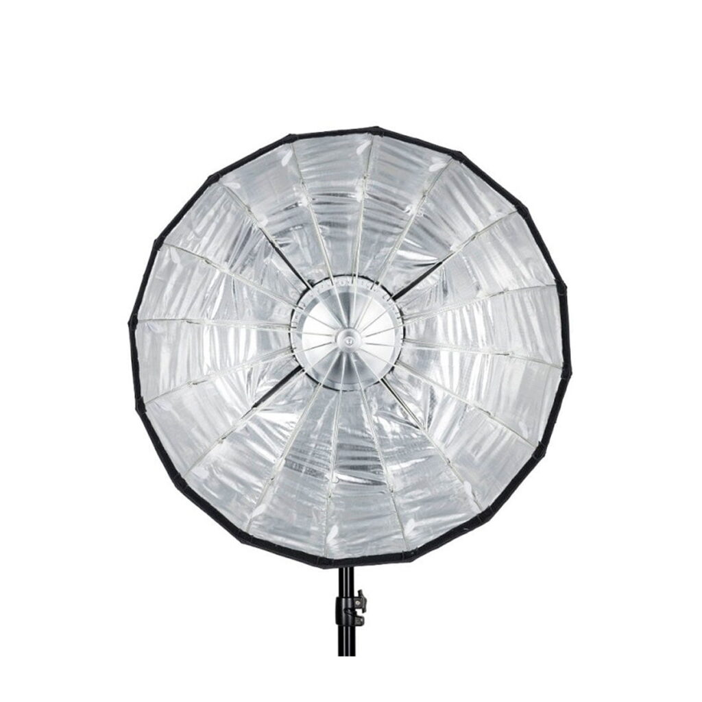 Quadralite_Flex_65cm_Foldable_Beauty-Dish_005 Quadralite Flex 65cm Foldable Beauty-Dish, suuri pyöreä hopeanvärinen softbox, jossa on heijastava sisus, on asennettu mustalle jalustalle ja sitä katsotaan edestä valkoista taustaa vasten.