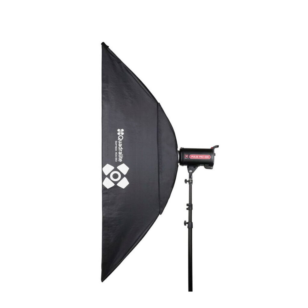 Quadralite_Softbox_40x180cm_002 Suorakulmainen Quadralite Softbox 40x180cm, musta, on asennettu jalustalle ja sitä katsotaan sivulta. Se on kiinnitetty salamalaitteeseen, joka on asetettu tavallista valkoista taustaa vasten.