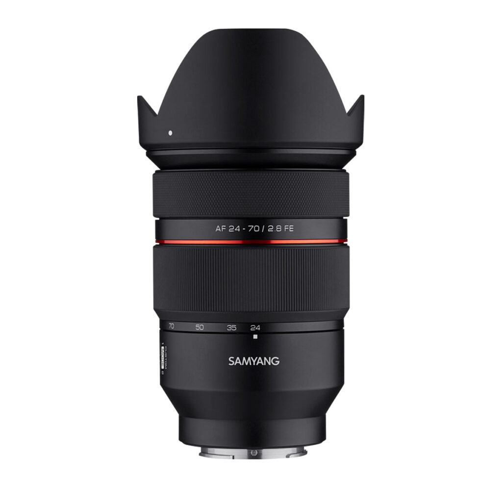 Samyang_AF_24-70mm_F_2_8_Sony_FE_001 Musta Samyang AF 24-70mm F/2.8 Sony FE -kameran objektiivi, jossa on terälehden muotoinen huppu, näkyvät zoomaus- ja tarkennusrenkaat, punainen aksenttirengas ja objektiivin kiinnitys alareunassa, eristettynä valkoiselle taustalle.
