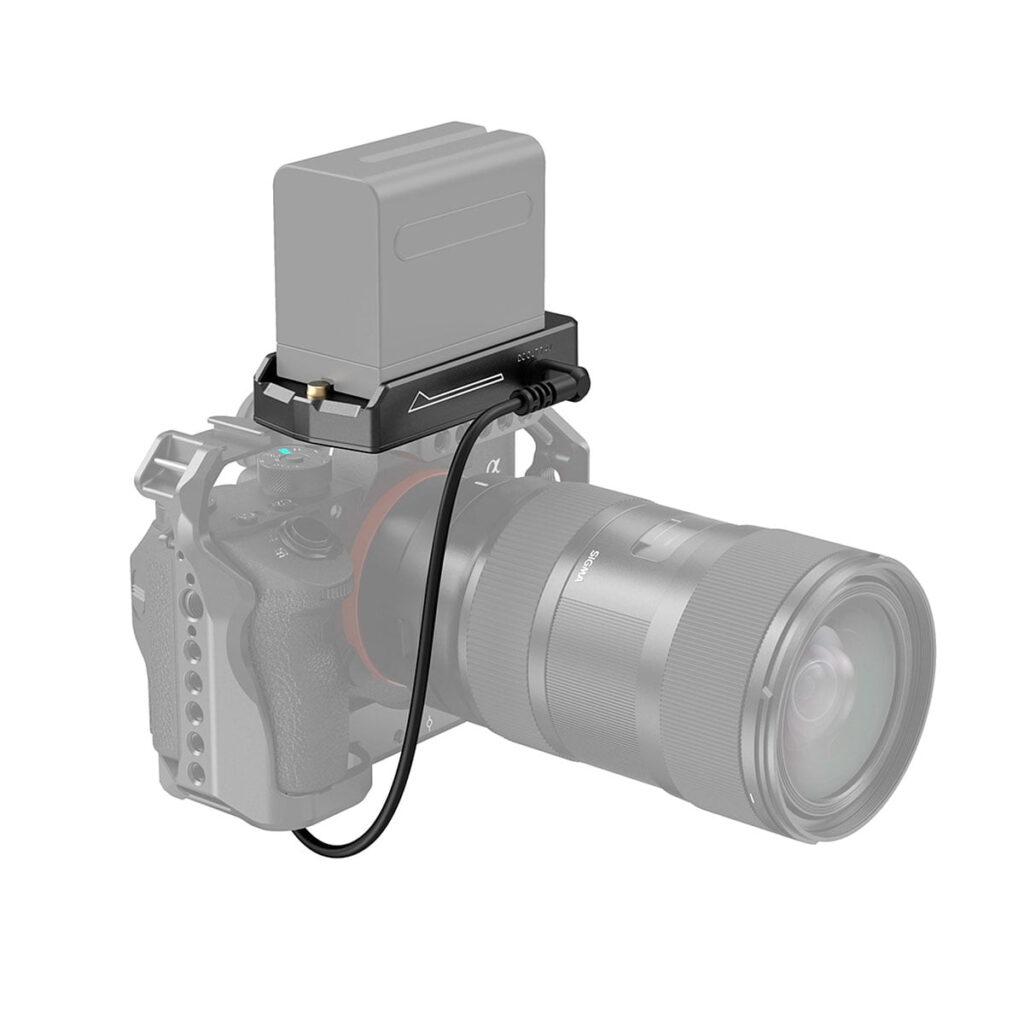 Suurella objektiivilla varustettu kamera on yhdistetty lyhyellä kaapelilla SmallRig 3095 NP-F Battery Adapter Plate Lite -akkusovitinlevyyn, jossa on NP-FZ100-nukkeakku, joka on asennettu päälle ja joka on kuvassa valkoista taustaa vasten.