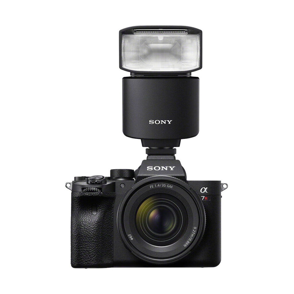 Sony_HVL-F46RM_010 Musta Sony-digitaalikamera, jossa on zoom-objektiivi ja suuri käsisalama, Sony HVL-F46RM, asennettuna päälle, kuvattuna valkoista taustaa vasten.