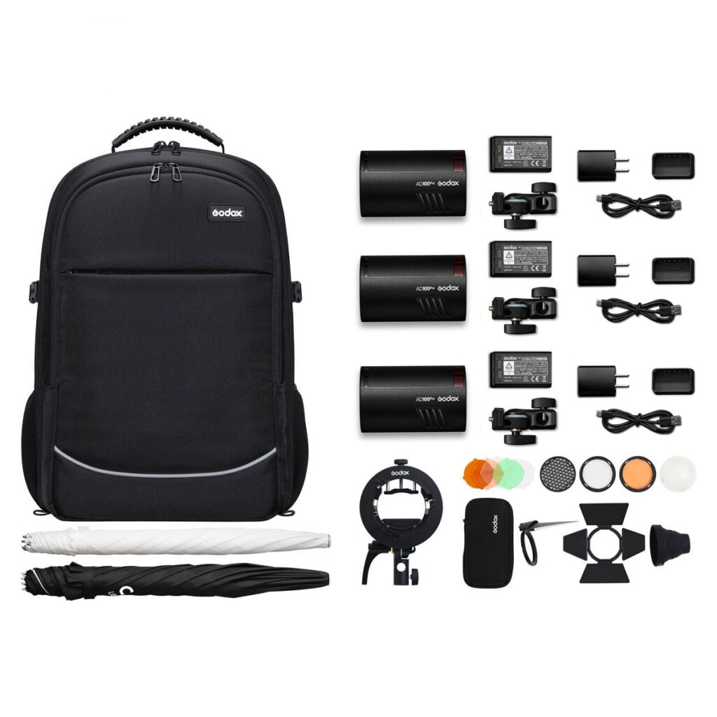 ad100pro_3backpack_01 Godox AD100 Pro TTL 3 salamaa -reppupakkaus sisältää mustan repun, kolme salamalaitetta, akut, laturit, sovittimet, valotelineen, värilliset suodattimet, diffuusorit, valkoisen sateenvarjon ja lisävarusteet - kaikki järjestetty siististi.