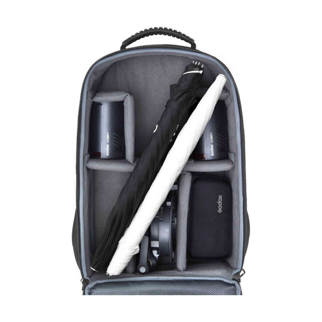 ad100pro_3backpack_03 Avoimessa Godox AD100 Pro TTL 3 salamaa -reppupaketissa, jossa on pehmustetut väliseinät, on kaksi kamerasalamaa, kierrejohto, vetoketjullinen pussi ja taitettu mustavalkoinen sateenvarjo.