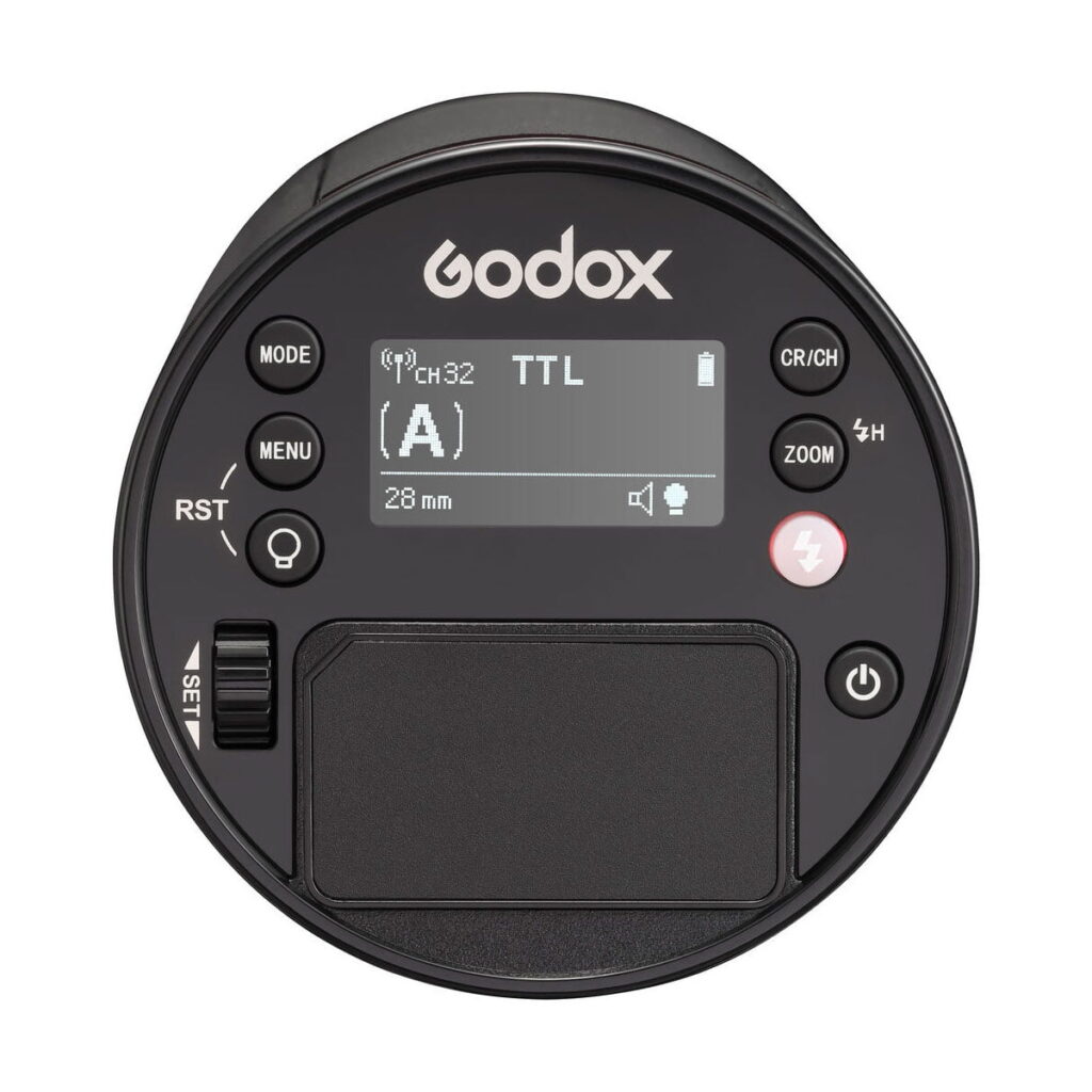 godox_ad100_pro_ttl_03 Yläkuvassa pyöreä Godox AD100 Pro TTL -akkusalama-salaman ohjausyksikkö, jossa on näyttö, painikkeita, valintakiekko ja merkittyjä ohjaimia tilalle, zoomille, valikolle ja virralle.