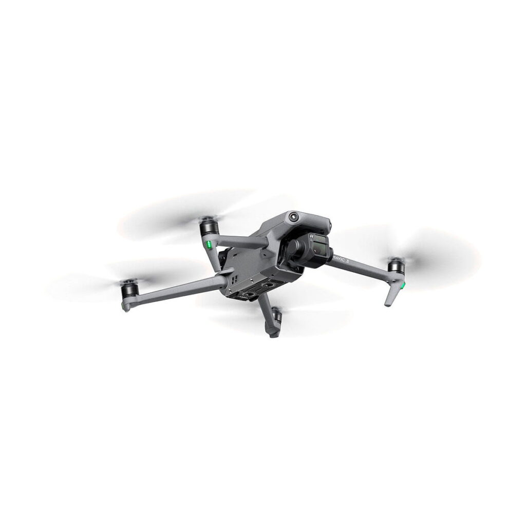 DJI_Mavic_3_Fly_More_Combo_009 DJI Mavic 3 Fly More Combo -lennokki, jossa on neljä potkuria, etukamera ja sensorit sekä pidennetyt laskeutumisjalat, lentää valkoista taustaa vasten.