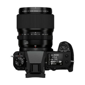 Fujifilm_GFX_100S_013 Ylhäältä katsottuna musta Fujifilm GFX 100S -järjestelmäkamera, jossa on suuri 80mm objektiivi, jossa näkyy säätöpyörät, painikkeet, elektroninen etsin ja näyttö, joka näyttää kuvausasetukset.
