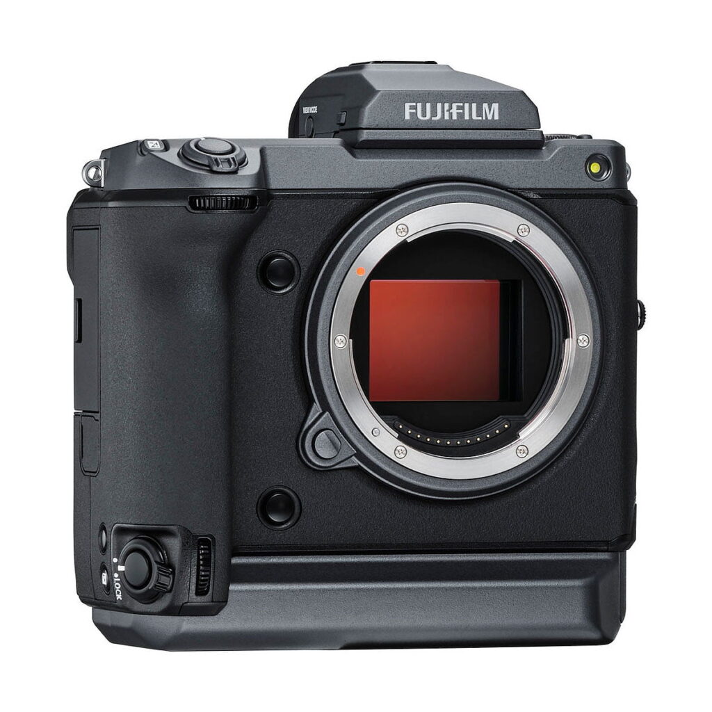 Fujifilm_GFX_100_001 Fujifilm GFX 100 on musta digitaalikameran runko, johon ei ole kiinnitetty objektiivia ja joka paljastaa kennon. Siinä on näkyvä vasemmanpuoleinen kahva sekä erilaisia ohjauspainikkeita ja valitsimia sen ylä- ja etupuolella.