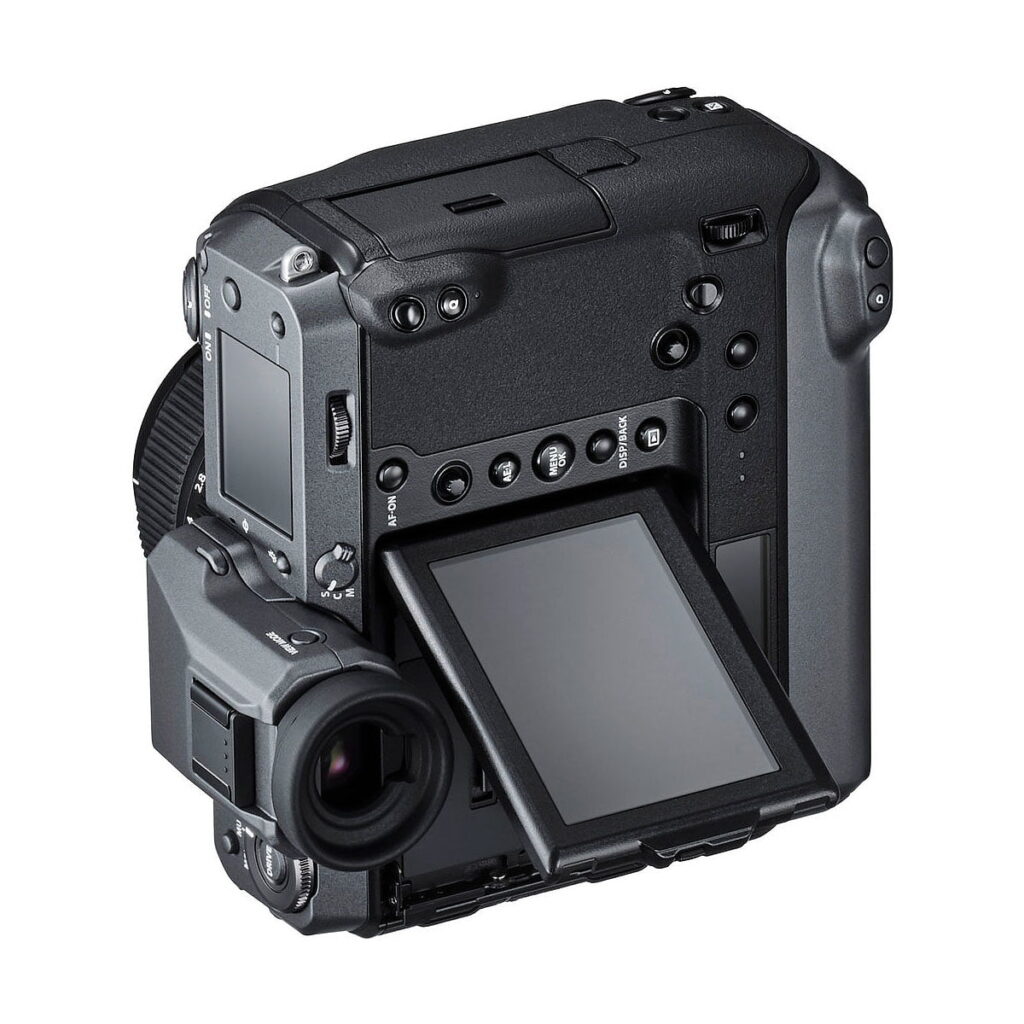 Fujifilm_GFX_100_006 Fujifilm GFX 100, musta digitaalikamera, jossa on suuri elektroninen etsin, kallistettu LCD-näyttö ja useita ohjauspainikkeita, on kuvattu takaa hieman vasemmalta valkoista taustaa vasten.