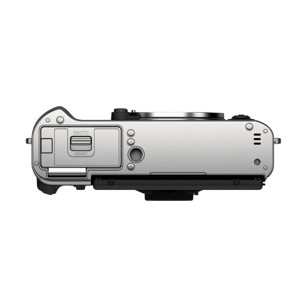 Fujifilm_X-T30_II__Hopea_004 Fujifilm X-T30 II Hopea hopeanvärisen digitaalikameran rungon ylhäältä, jossa näkyy akkulokeron luukku, säätimet, painikkeet, objektiivin kiinnitys ja portit. Kamera on asetettu valkoista taustaa vasten.