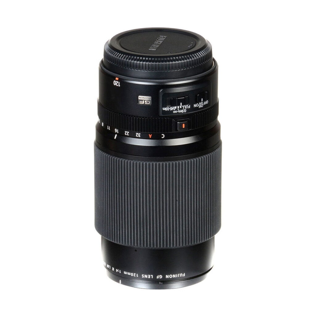 Fujifilm Fujinon GF 120mm f/4 Macro R LM OIS WR -objektiivi mustana, jossa on kuvioitu tarkennusrengas, aukon merkinnät ja objektiivin suojus, seisoo pystyssä valkoisella taustalla.