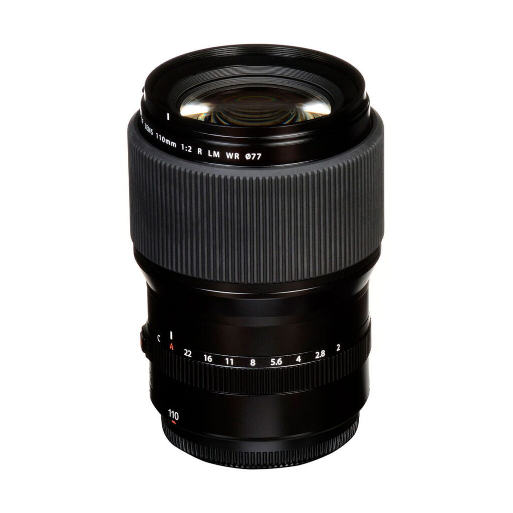 Fujifilm Fujinon GF 110mm f/2 R LM WR -objektiivi on musta kameraobjektiivi, jossa on kuvioitu kahva, näkyvät lasielementit ja aukkomerkinnät tarkennusrenkaassa valkoista taustaa vasten.