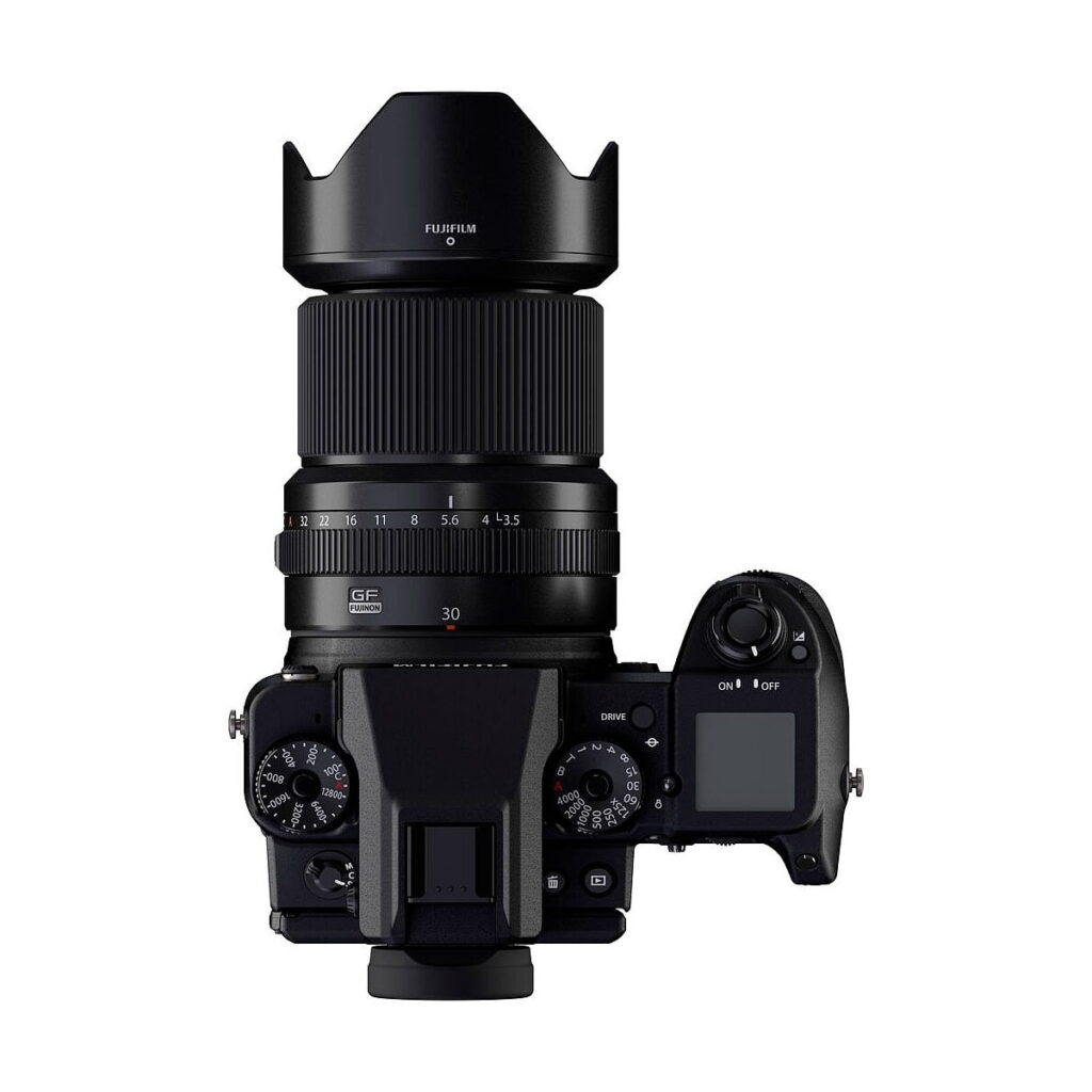 Ylhäältä katsottuna musta Fujifilm-kamera, jossa on Fujinon GF 30mm f/3.5 R WR -objektiivi, jossa on suuri objektiivi ja huppu, näkyvät säätöpyörät, painikkeet ja LCD-näyttö oikealla puolella.