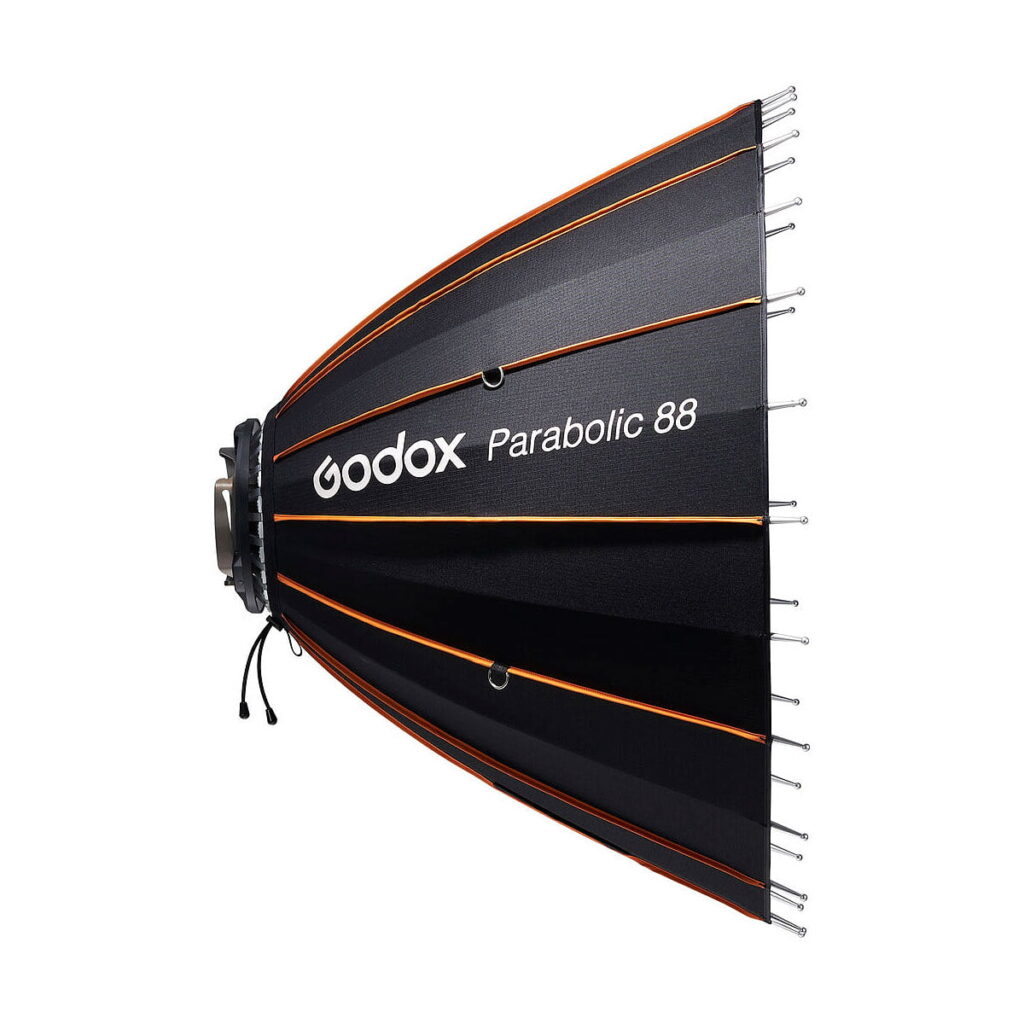 Godox_Parabolic_88_Reflector_Kit_004 Sivukuva Godox Parabolic 88 -heijastinsarjasta, jossa on mustat kangaspaneelit oransseilla korostuksilla ja hopeisilla tangoilla, jotka on suunniteltu valokuvausvalaistukseen. Mallin nimi on painettu kylkeen.