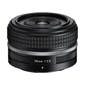 Nikon_Nikkor_Z_28mm_f_2_8_001 Nikon Nikkor Z 28mm f/2.8 SE -objektiivi on musta kameraobjektiivi, jossa on kuvioitu tarkennusrengas ja hopeinen korostus valkoista taustaa vasten.