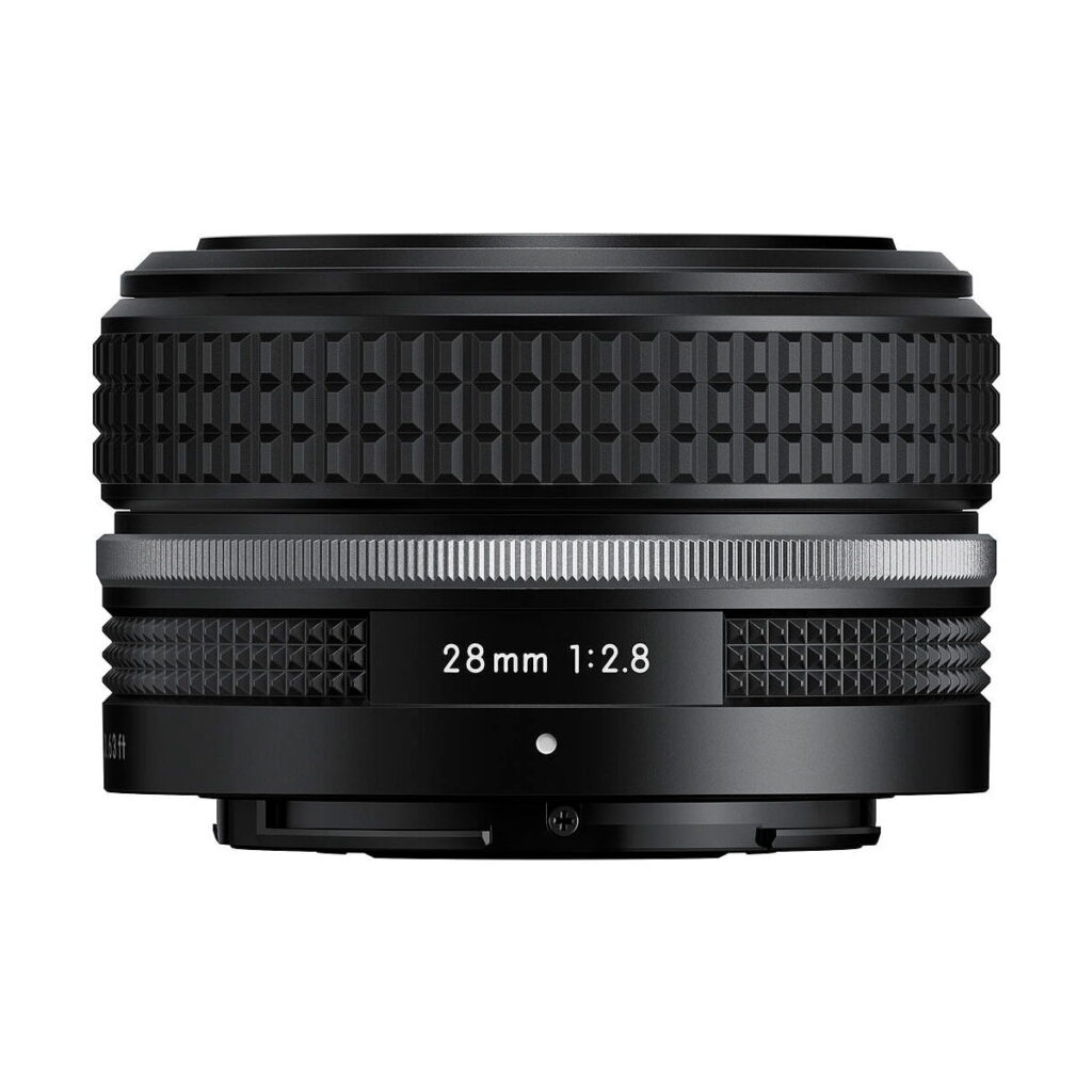 Nikon_Nikkor_Z_28mm_f_2_8_002 A Nikon Nikkor Z 28mm f/2.8 SE -objektiivi musta kameran objektiivi, jossa on kuvioitu otepinta ja toivottu rengas, jossa lukee 28mm 1:2.8. Objektiivia katsellaan sivulta valkoista taustaa vasten.