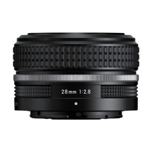 Nikon_Nikkor_Z_28mm_f_2_8_002 A Nikon Nikkor Z 28mm f/2.8 SE -objektiivi musta kameran objektiivi, jossa on kuvioitu otepinta ja toivottu rengas, jossa lukee 28mm 1:2.8. Objektiivia katsellaan sivulta valkoista taustaa vasten.