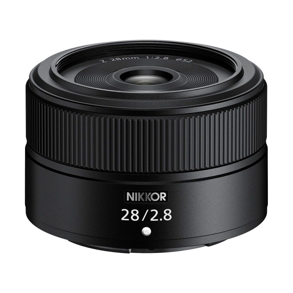 Nikon_Nikkor_Z_28mm_f_2_8_standard_001 Nikon Nikkor Z 28mm f/2.8 -objektiivi, musta, jossa on merkintä "Z 28mm 1:2.8", jossa on leveä etulasi ja harjakuvioinen tarkennusrengas ja joka on esillä valkoista taustaa vasten.