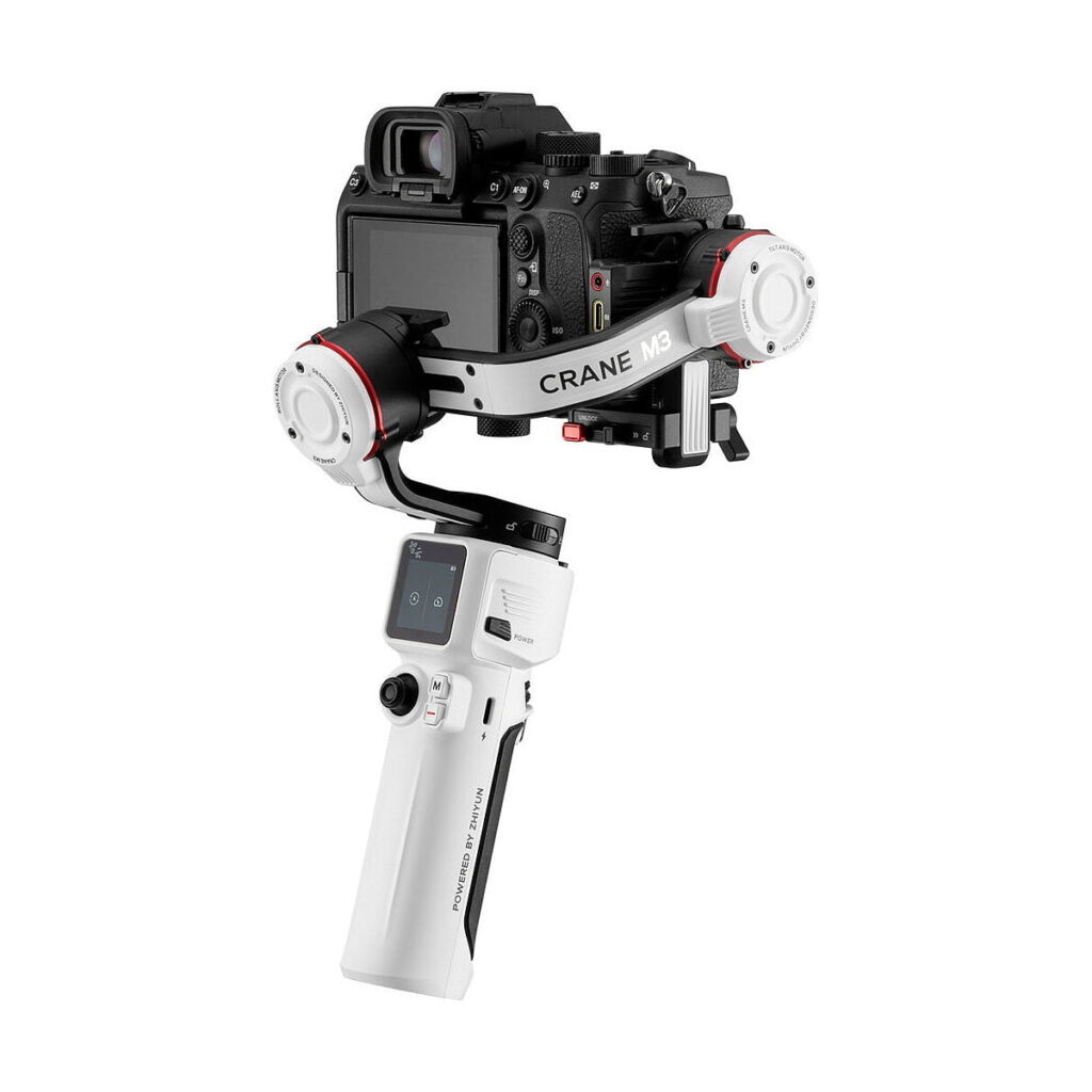 Zhiyun-Tech_Crane_M3_001 Musta digitaalikamera on kiinnitetty valkoiseen Zhiyun Crane M3 - Gimbaali -käsivakaajaan, jonka kahvassa on pieni näyttö ja ohjauspainikkeet.