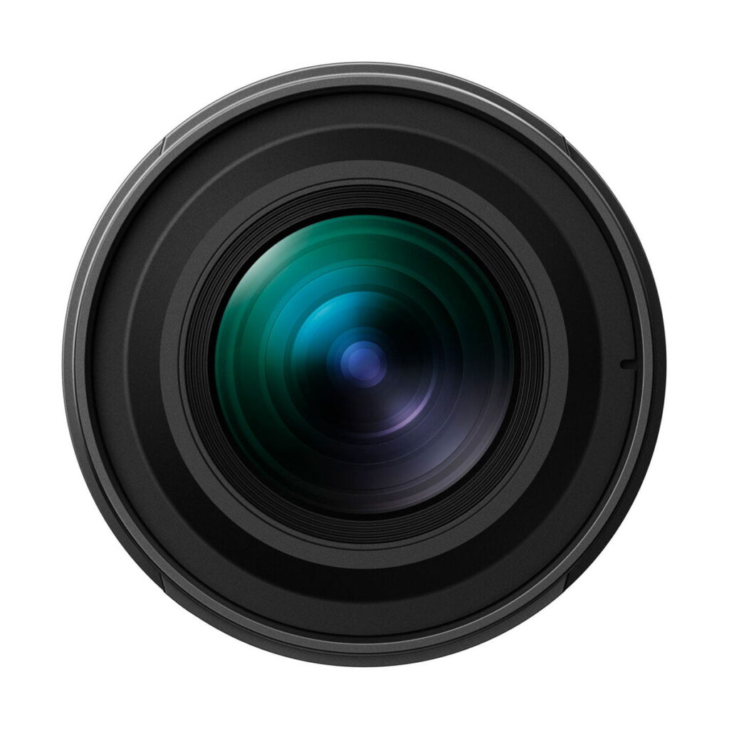 om_systems_20mm_f14_pro_05 Lähikuva OM SYSTEM M.Zuiko Digital ED 20mm f/1.4 PRO -objektiivi -objektiivista, jossa näkyvät valkoista taustaa vasten näkyvät samankeskiset renkaat ja lasiheijastukset, joiden keskellä on vihreitä ja sinisiä korostuksia.